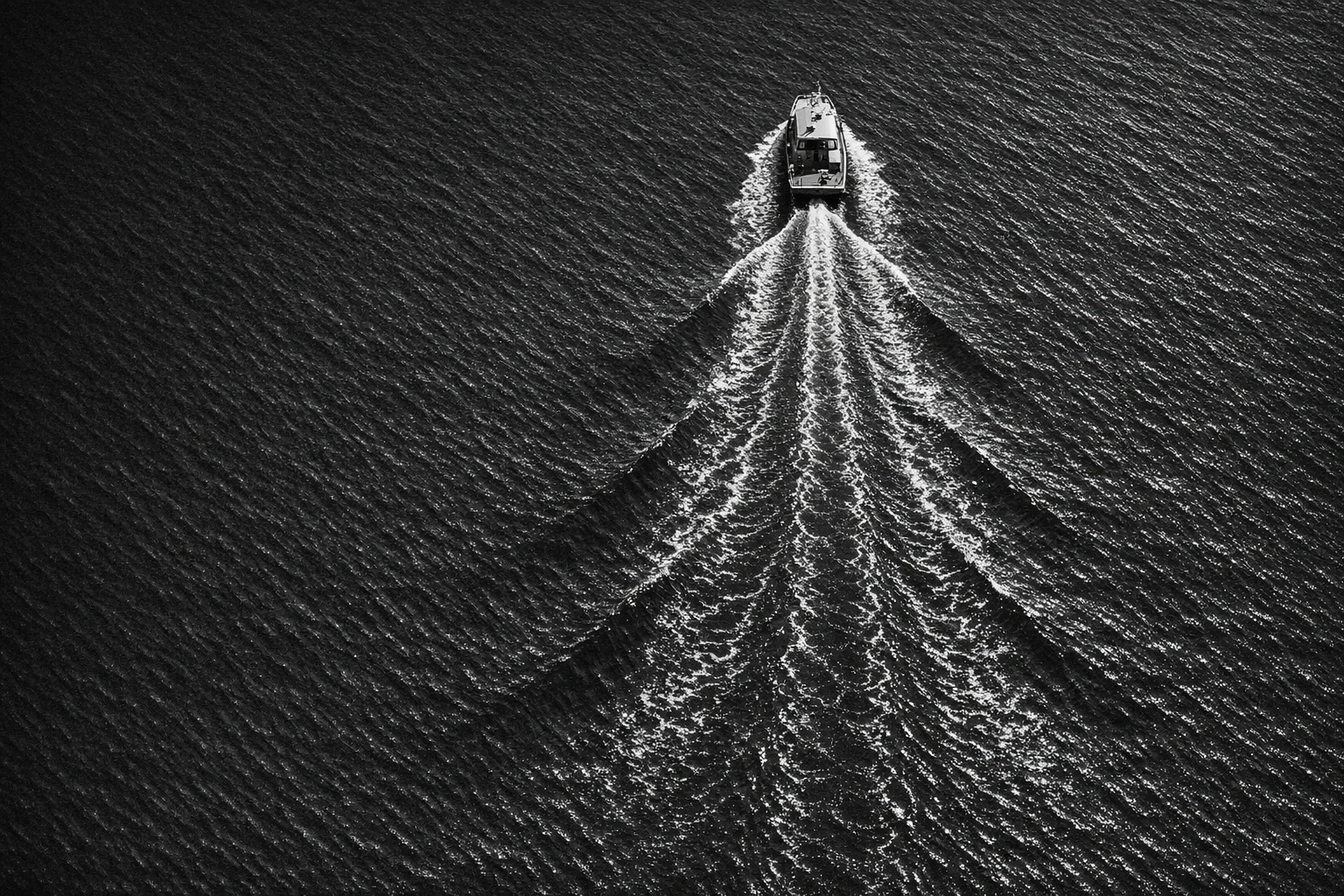 Aerial black-and-white view of a survey craft leaving a directional wake